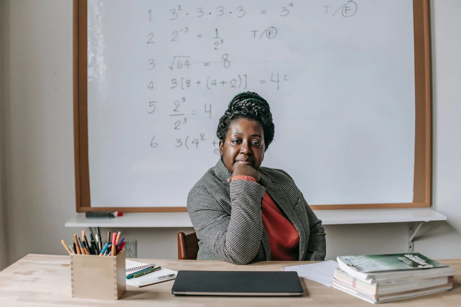 A teacher seated at a desk in front of a classroom board